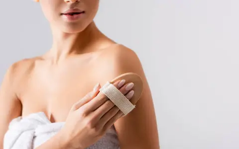 Donna usa una spazzola per il corpo per esfoliare la pelle, un segreto per come mantenere abbronzatura a lungo.