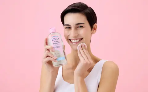 Donna sorridente con acqua micellare Lycia e dischetto di cotone, perfetta per imparare come pulire il viso quotidianamente.