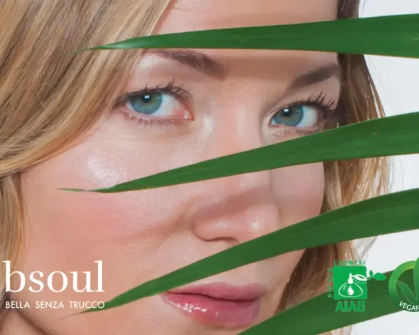 Occhi azzurri e pelle luminosa di una donna, con foglie verdi che creano un effetto di trasparenza, suggerendo un approccio naturale contro l'invecchiamento precoce.