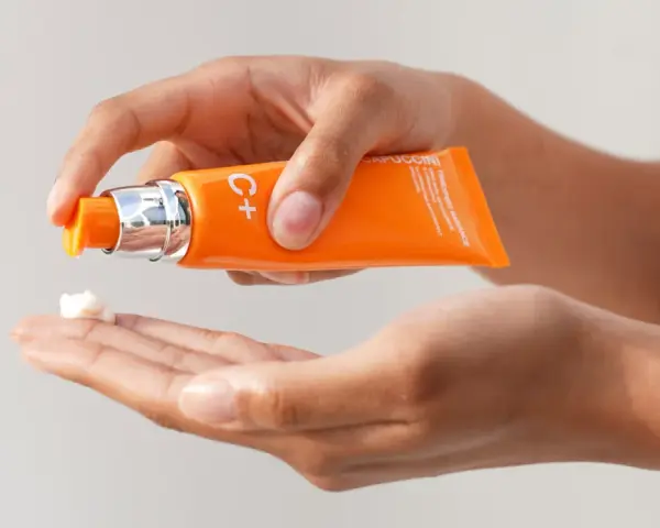 Mani che dosano crema viso con vitamina C, per illuminare e proteggere la pelle.