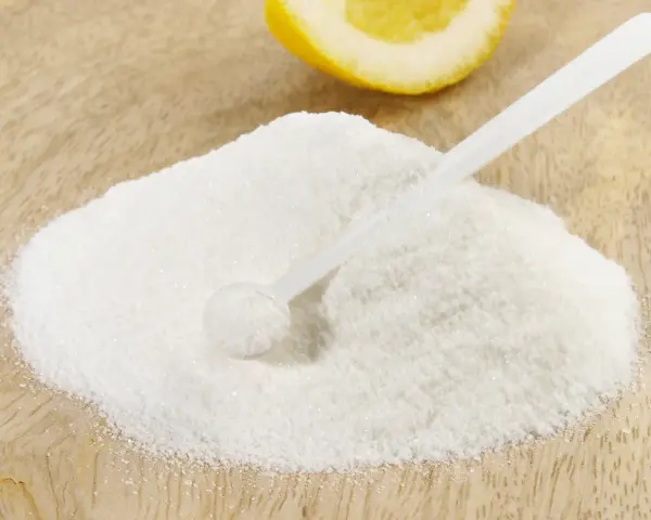 Polvere bianca, forse acido citrico, con un cucchiaino e una fetta di limone sullo sfondo. Ideale per la vitamina C.