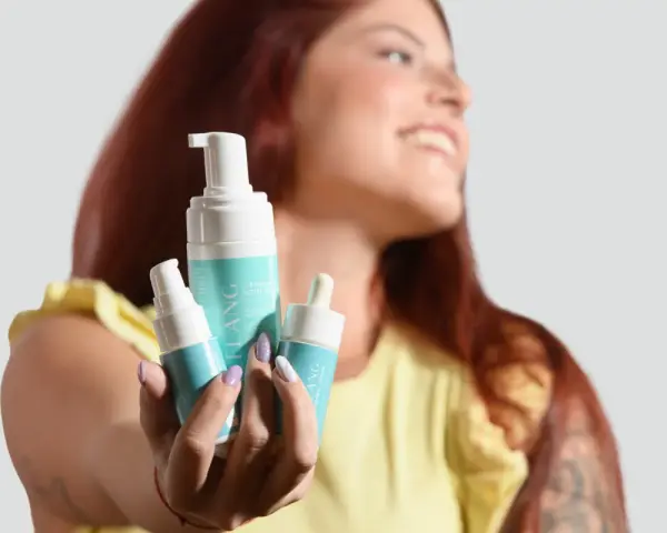 Donna sorridente mostra prodotti per skincare mattina: mousse detergente e siero.