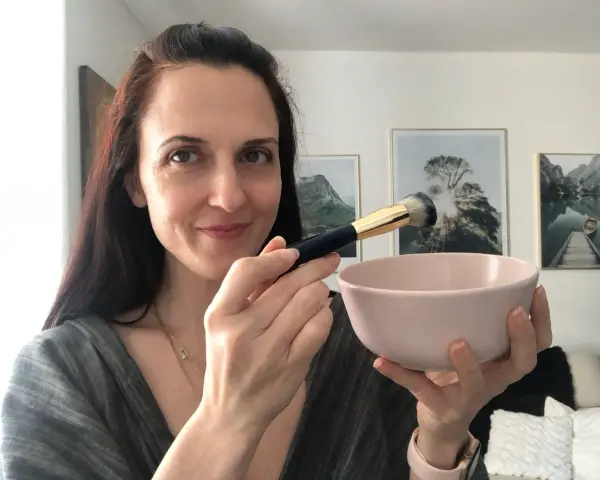 Donna prepara una maschera viso fai da te con bicarbonato, usando un pennello per applicarla.