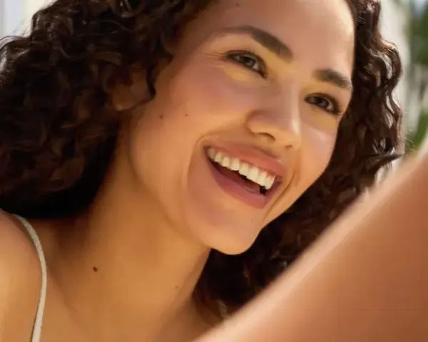 Donna sorridente con riccioli scuri, un esempio di come avere un viso più bello con un sorriso radioso e una pelle luminosa.