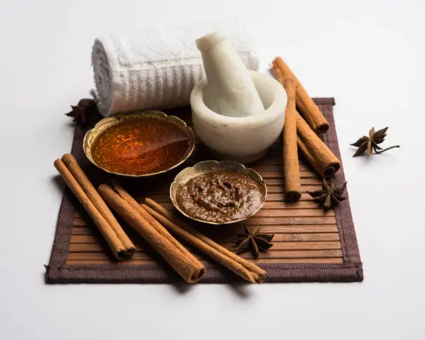 Ingredienti per una maschera al miele antirughe: miele dorato, cannella, anice stellato, mortaio e asciugamano arrotolato.