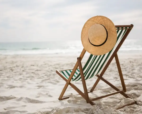 Spiaggia deserta con sdraio e cappello di paglia. Ricorda i rimedi per il colpo di calore: idratarsi e cercare l'ombra.