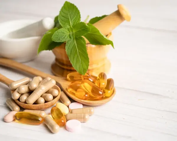 Cucchiaio con capsule e pillole, tra cui quelle contenenti tocoferolo dove si trova, accanto a un mortaio con menta.