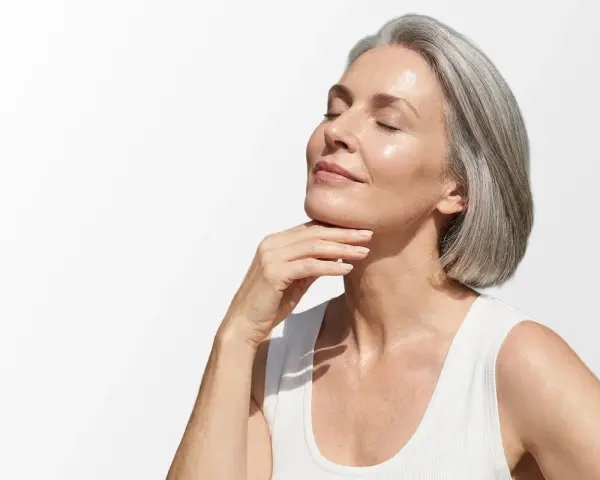 Donna con capelli grigi e pelle luminosa, che accarezza il collo. Scopri i migliori rimedi per le rughe del collo.