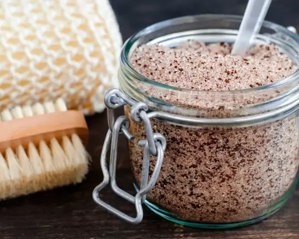 Un barattolo di scrub miele e zucchero, con una spazzola e una spugna per il corpo.