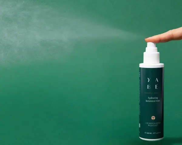 Dito come si usa il tonico viso: una mano spruzza il tonico idratante YABE su sfondo verde.