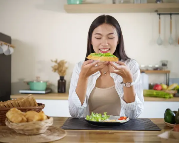 Donna assapora un toast con avocado, un alimento ricco di vitamina E, essenziale per la pelle e il sistema immunitario.