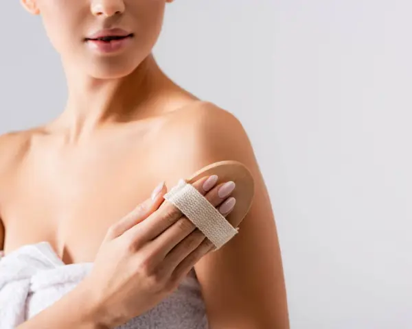 Donna usa una spazzola per il corpo per esfoliare la pelle, un segreto per come mantenere abbronzatura a lungo.