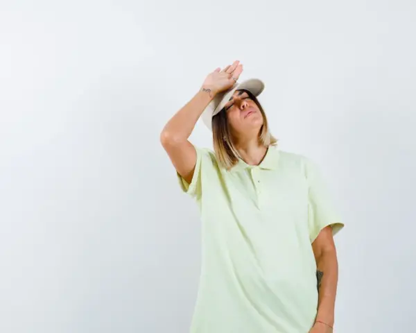 Donna con cappellino e maglietta chiara, mano sulla fronte, con espressione di chi soffre per l'insolazione quanto dura.