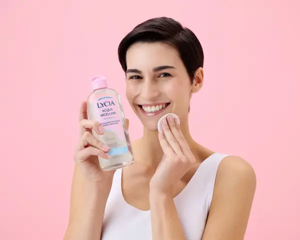 Donna sorridente con acqua micellare Lycia e dischetto di cotone, perfetta per imparare come pulire il viso quotidianamente.