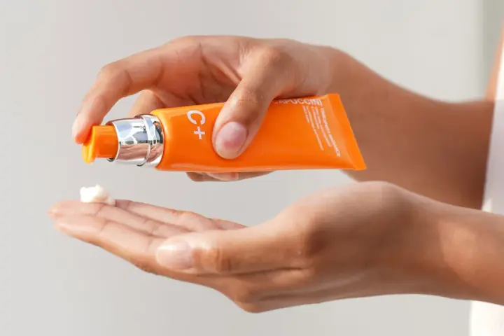 Mani che dosano crema viso con vitamina C, per illuminare e proteggere la pelle.
