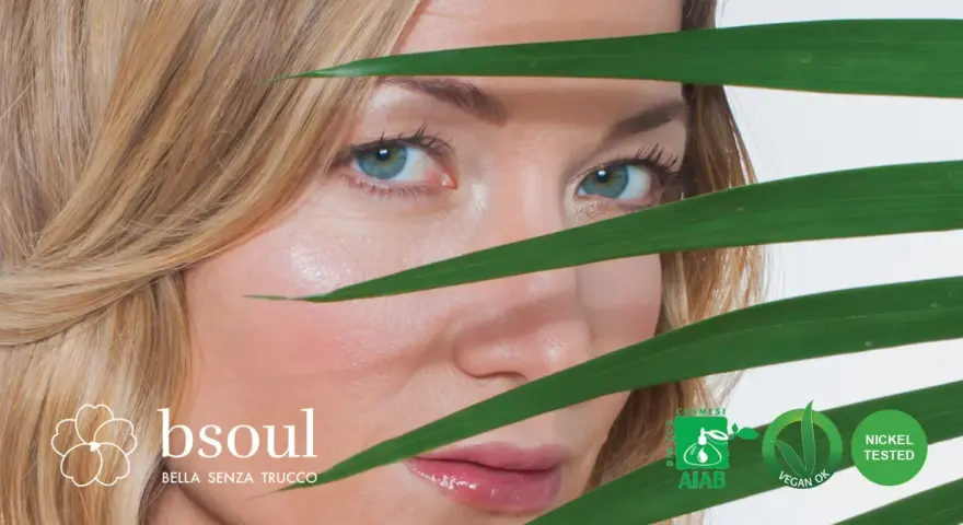 Occhi azzurri e pelle luminosa di una donna, con foglie verdi che creano un effetto di trasparenza, suggerendo un approccio naturale contro l'invecchiamento precoce.