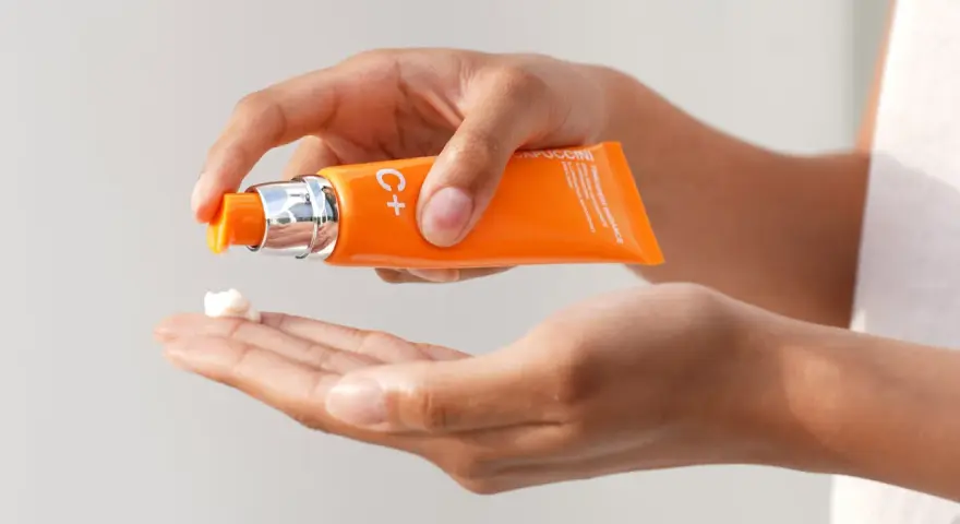 Mani che dosano crema viso con vitamina C, per illuminare e proteggere la pelle.
