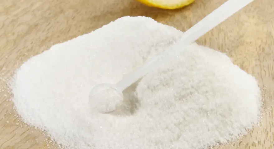 Polvere bianca, forse acido citrico, con un cucchiaino e una fetta di limone sullo sfondo. Ideale per la vitamina C.