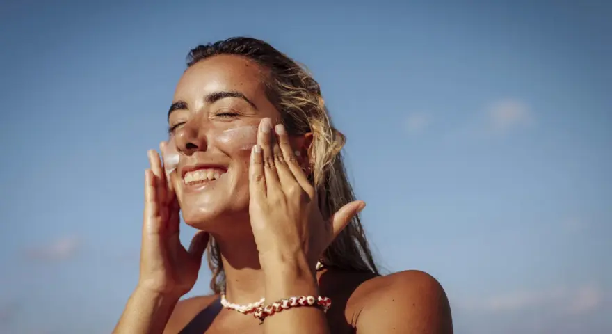 Donna sorridente applica crema solare per proteggere la pelle da macchie e tumore.