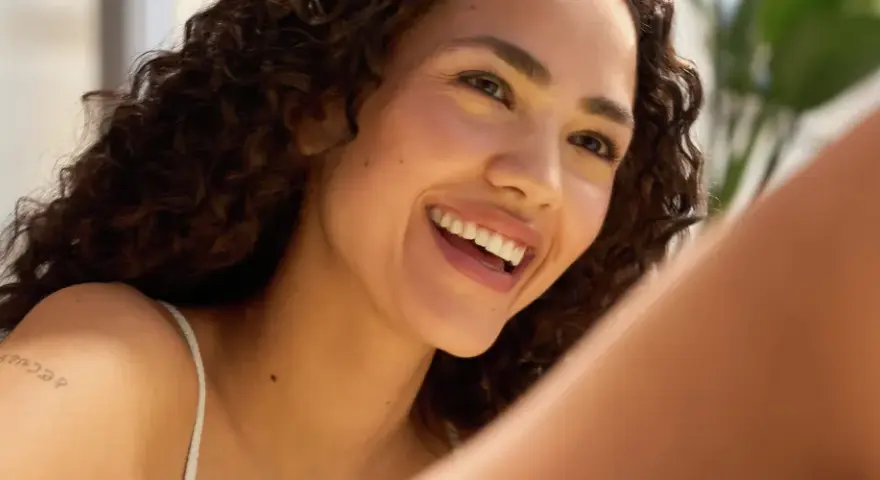 Donna sorridente con riccioli scuri, un esempio di come avere un viso più bello con un sorriso radioso e una pelle luminosa.