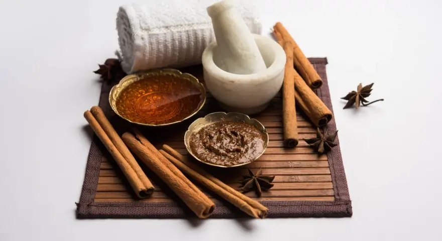 Ingredienti per una maschera al miele antirughe: miele dorato, cannella, anice stellato, mortaio e asciugamano arrotolato.