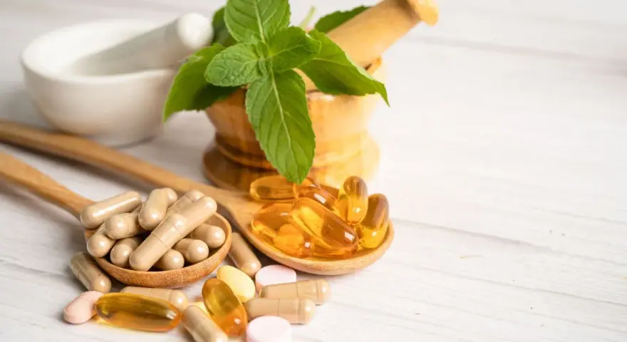 Cucchiaio con capsule e pillole, tra cui quelle contenenti tocoferolo dove si trova, accanto a un mortaio con menta.