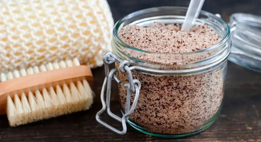 Un barattolo di scrub miele e zucchero, con una spazzola e una spugna per il corpo.
