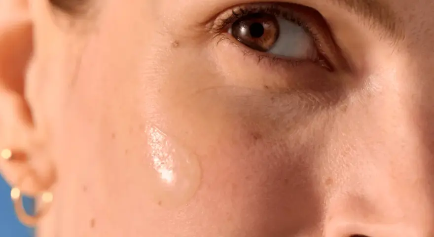 Goccia di siero su pelle abbronzata con delicati puntini bianchi visibili.