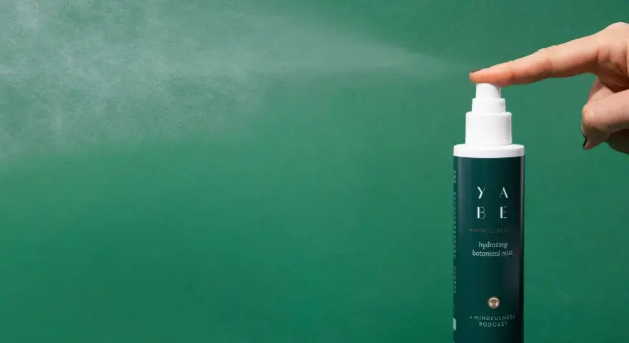 Dito come si usa il tonico viso: una mano spruzza il tonico idratante YABE su sfondo verde.