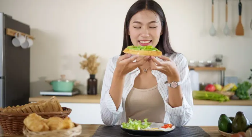 Donna assapora un toast con avocado, un alimento ricco di vitamina E, essenziale per la pelle e il sistema immunitario.