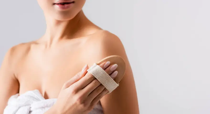 Donna usa una spazzola per il corpo per esfoliare la pelle, un segreto per come mantenere abbronzatura a lungo.