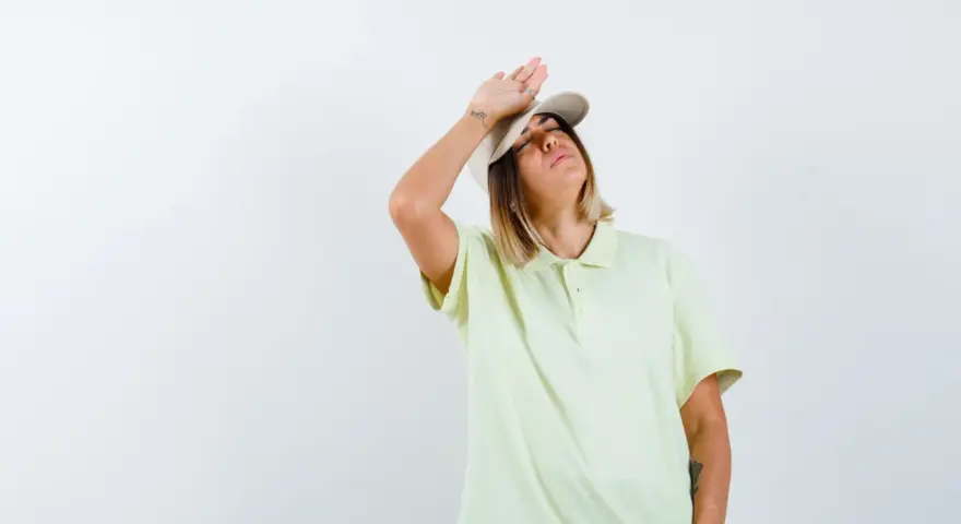 Donna con cappellino e maglietta chiara, mano sulla fronte, con espressione di chi soffre per l'insolazione quanto dura.