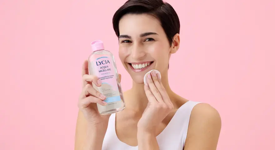 Donna sorridente con acqua micellare Lycia e dischetto di cotone, perfetta per imparare come pulire il viso quotidianamente.