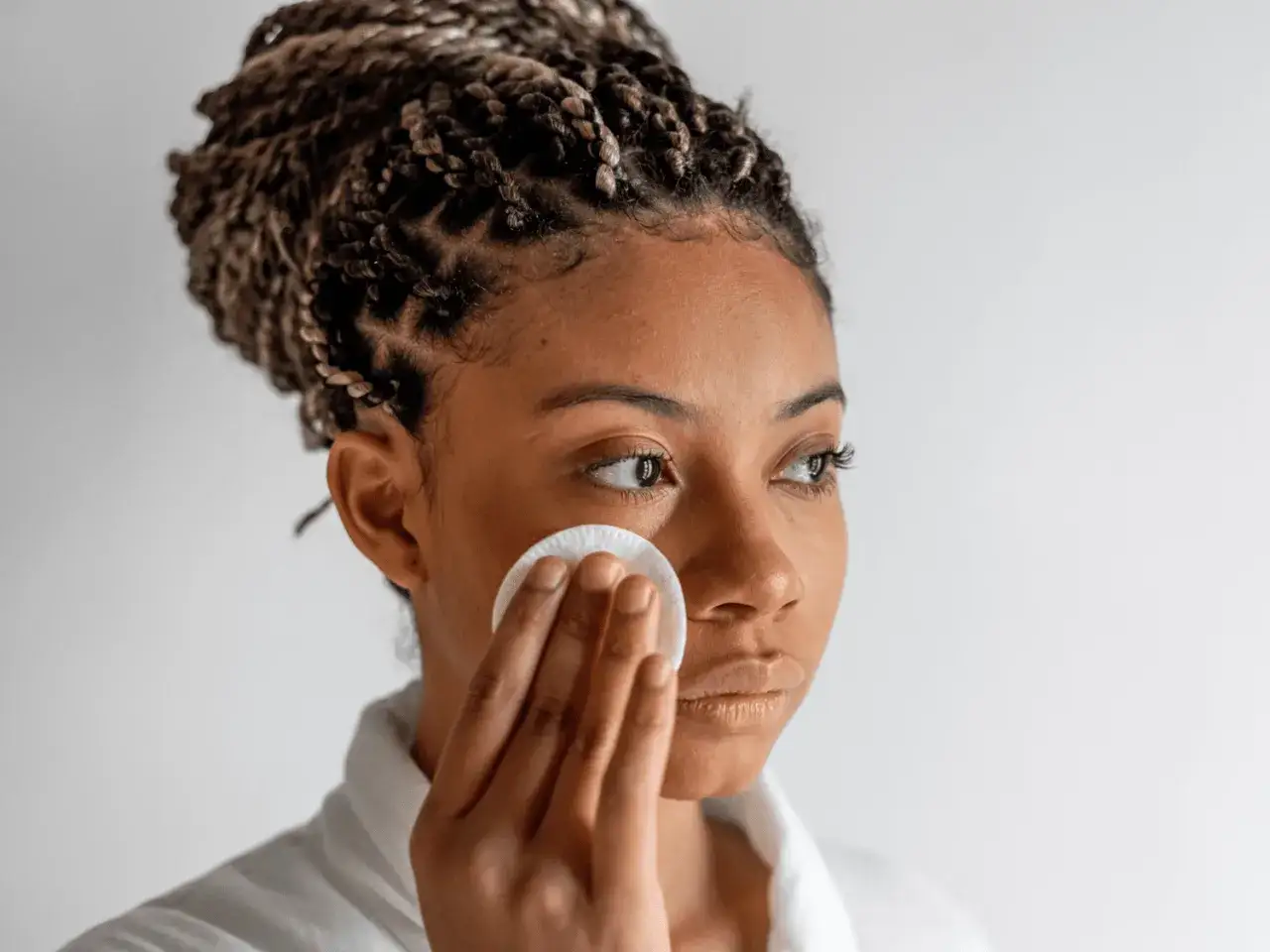 Donna con treccine applica tonico viso con un dischetto di cotone, un gesto semplice per una pelle fresca.