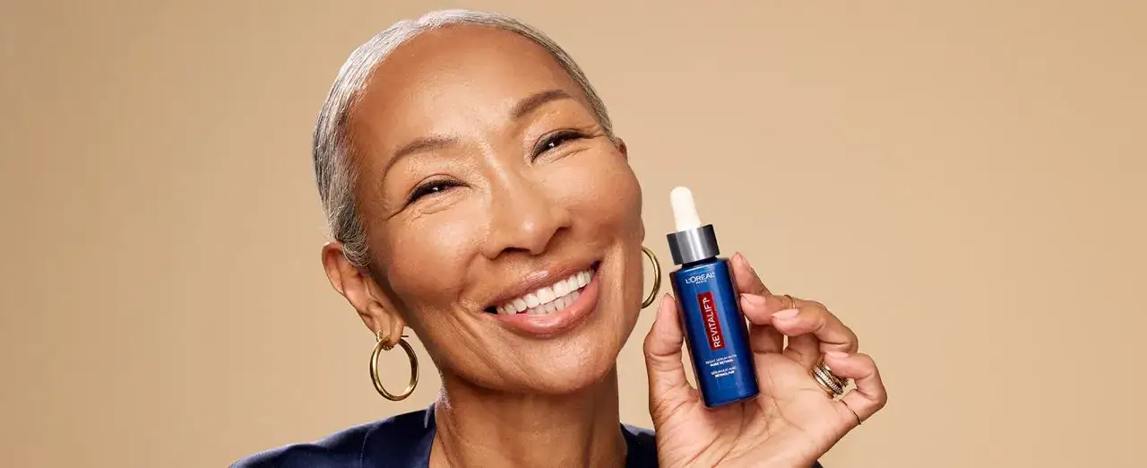 Donna sorridente mostra un siero viso L'Or&eacute;al Revitalift. Il retinolo cosa serve? A rigenerare la pelle, riducendo rughe e segni del tempo.
