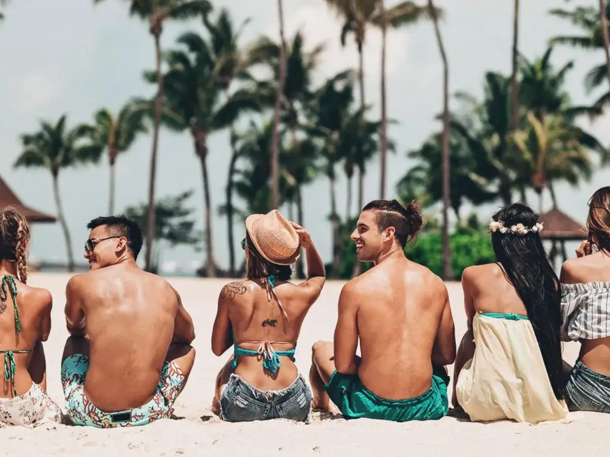Amici in spiaggia, la loro pelle abbronzata mostra la melanina cos'&egrave;: protezione solare naturale. Palme sullo sfondo.
