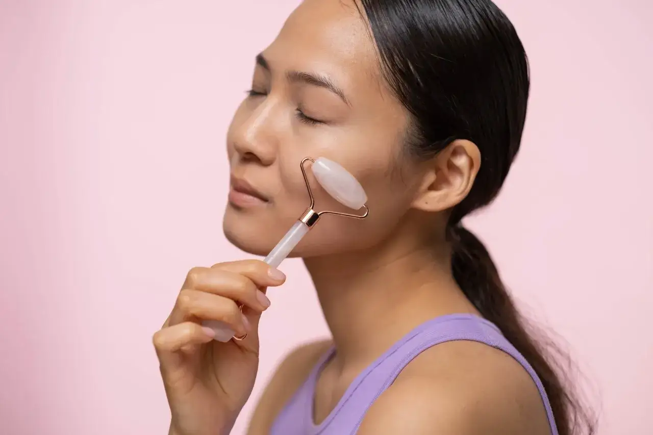 Donna usa un rullo di quarzo rosa per massaggiare il viso, un rimedio naturale per la pelle del viso cadente.