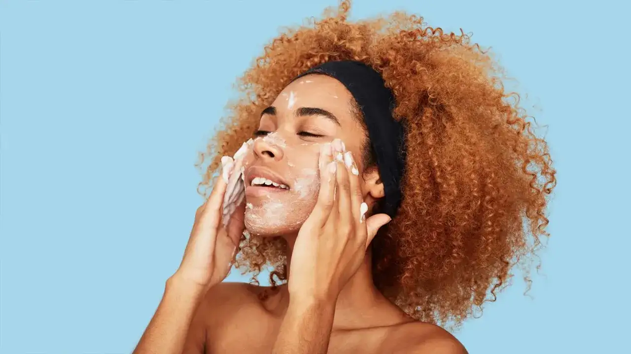 Donna con capelli ricci e fascia nera si lava il viso con schiuma detergente. Dopo il latte detergente il viso va lavato per una pulizia profonda.