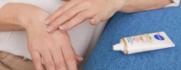 Mani che si toccano, alleviando rossore e prurito tra le dita. Accanto, un tubetto di crema Nivea.