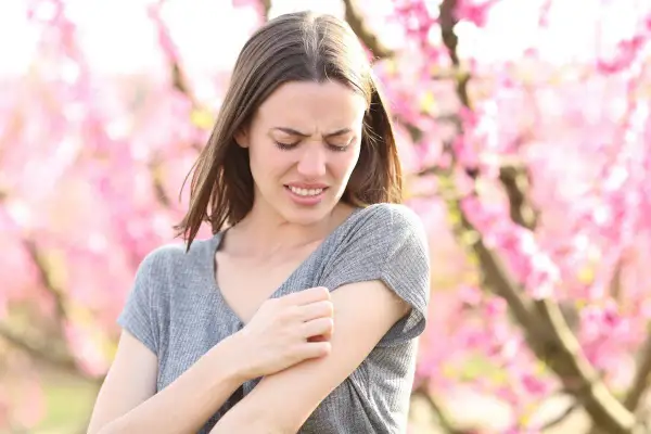 Donna con prurito in tutto il corpo, graffiandosi il braccio tra i fiori rosa.